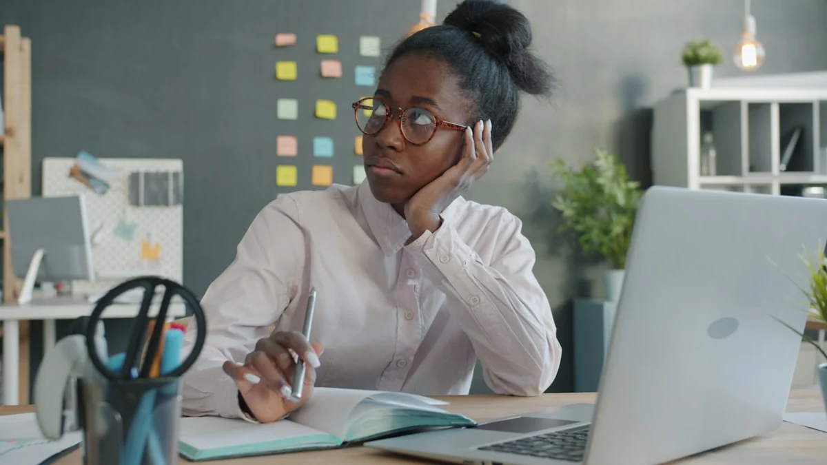 Serious African American businesswoman is thinking and looking around sitting at desk in office. Businesspeople, workplace and emotions concept.